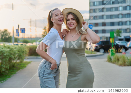 Two smiling young female friends standing on city street in summer Two smiling young female friends standing on city street in summer 142962993