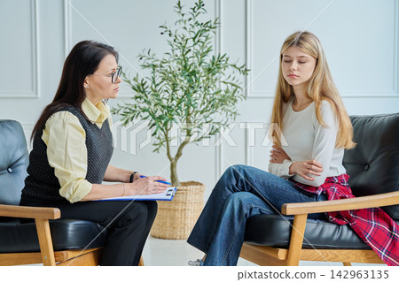 Professional female psychologist counseling sad teenager girl in office Professional female psychologist counseling sad teenager girl in office 142963135