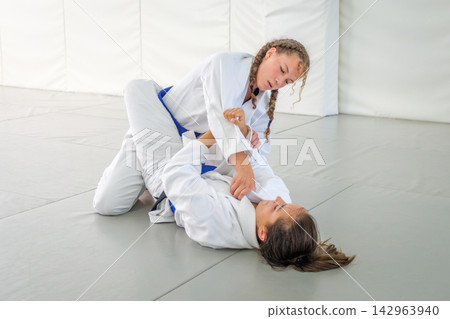 Two female athletes grappling in jiu jitsu guard position Two female athletes grappling in jiu jitsu guard position 142963940