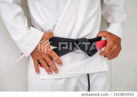Close up of a tied jiu jitsu black belt and red rank bar Close up of a tied jiu jitsu black belt and red rank bar 142963950