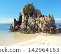 Rugged rock formation rises from sandy shore 142964163
