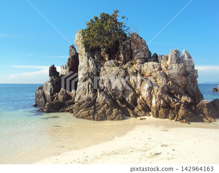 Rugged rock formation rises from sandy shore Rugged rock formation rises from sandy shore 142964163