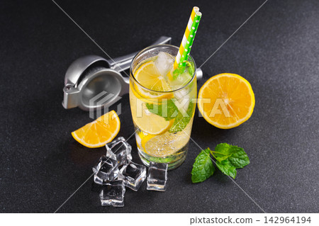 Cold homemade lemonade with fresh lemon, mint and ice in glass on black textured stone background Cold homemade lemonade with fresh lemon, mint and ice in glass on black textured stone background 142964194