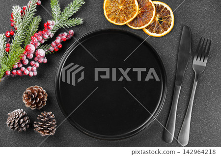 Christmas table setting with empty black plate, silver cutlery and holiday decor on dark background Christmas table setting with empty black plate, silver cutlery and holiday decor on dark background 142964218