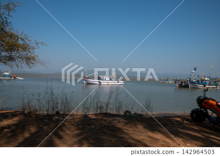 Harbor for small fishing vessels in Karnataka, India (or Kerala, Maharashtra, Goa). Unrecognizable fishermen (motion blur) in the distance on moored fishing boats. Numerous small brahminy kites fly ov Harbor for small fishing vessels in Karnataka, India (or Kerala, Maharashtra, Goa). Unrecognizable fishermen (motion blur) in the distance on moored fishing boats. Numerous small brahminy kites fly ov 142964503