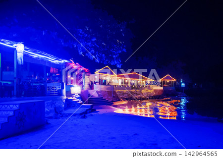 Cafe on the beach in the night - reflections of neon colors in water on coastline in Goa Cafe on the beach in the night - reflections of neon colors in water on coastline in Goa 142964565