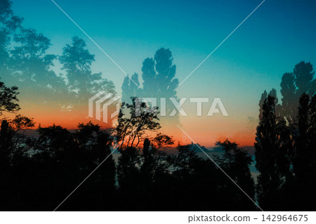 Layered tree silhouettes rise against a vivid sunset sky, blending cyan blue and warm orange tones into a dreamy atmospheric landscape with a cinematic mood, depth, contrast and serene natural beauty. Layered tree silhouettes rise against a vivid sunset sky, blending cyan blue and warm orange tones into a dreamy atmospheric landscape with a cinematic mood, depth, contrast and serene natural beauty. 142964675