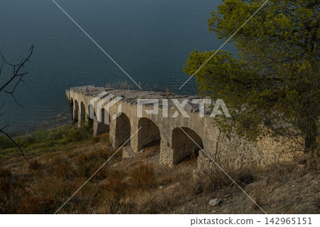 Old stone arch aqueduct ruins by the turquoise Amadorio Reservoir in Spain showcase history and nature together Old stone arch aqueduct ruins by the turquoise Amadorio Reservoir in Spain showcase history and nature together 142965151