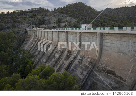 Wide shot of Amadorio Dam with curved concrete structure surrounded by pine trees and mountains Wide shot of Amadorio Dam with curved concrete structure surrounded by pine trees and mountains 142965168