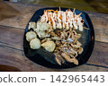 Close up view of Asian style chicken teriyaki sprinkled with sesame seeds, fresh salad with sauce, and deep-fried side dishes served on a dark plate over a wooden table. 142965443
