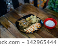 Asian style chicken set meal served with steamed white rice in a bowl, fresh salad with sauce, and deep-fried side dishes on a dark plate over a wooden table. 142965444