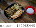 Asian style chicken set meal served with steamed white rice in a bowl, fresh salad with sauce, and deep-fried side dishes on a dark plate over a wooden table. 142965445