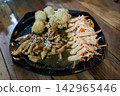 Close up view of Asian style chicken teriyaki sprinkled with sesame seeds, fresh salad with sauce, and deep-fried side dishes served on a dark plate over a wooden table. 142965446