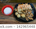 Asian style chicken set meal served with steamed white rice in a bowl, fresh salad with sauce, and deep-fried side dishes on a dark plate over a wooden table. 142965448
