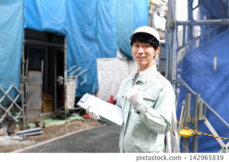一名微笑的亞洲工人在建築工地擺出勝利姿勢。 一名微笑的亞洲工人在建築工地擺出勝利姿勢。 142965839