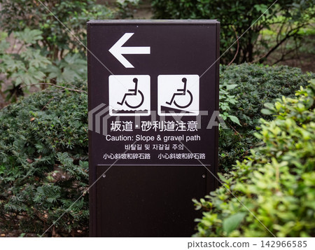 A multilingual sign with a wheelchair symbol warning of "Slope/Gravel Road Caution" A multilingual sign with a wheelchair symbol warning of "Slope/Gravel Road Caution" 142966585