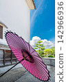 A Japanese umbrella stands out quietly in front of a white-walled storehouse. 142966936