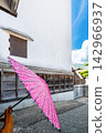 A Japanese umbrella stands out quietly in front of a white-walled storehouse. 142966937