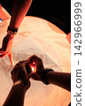 Low Angle Close Up of Hands Cooperating to Light a Sky Lantern at Night Festival 142966999
