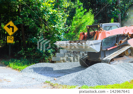 Construction vehicle spreads gravel on road near left turn sign, stones are work area Construction vehicle spreads gravel on road near left turn sign, stones are work area 142967641