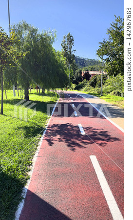 Red bike path park infrastructure background. Bicycle lane outdoor summer recreation. Fun fitness hobby active lifestyle backdrop. Red bike path park infrastructure background. Bicycle lane outdoor summer recreation. Fun fitness hobby active lifestyle backdrop. 142967683