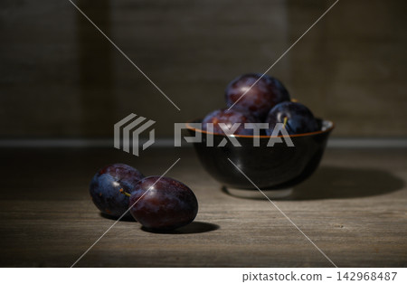 Commercial stock photo of fresh dark purple plums in a bowl and on a wooden table Commercial stock photo of fresh dark purple plums in a bowl and on a wooden table 142968487