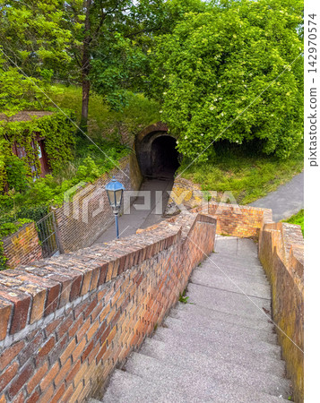 stone stairs leading down along a brick wall toward a vintage street lamp. 142970574