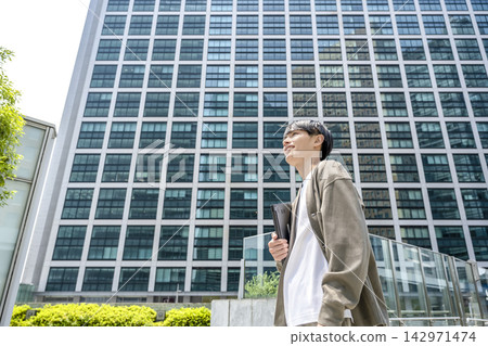 一名年輕男子帶著筆記型電腦走在新橋街頭。 142971474