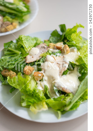 Caesar salad, lettuce, chicken, creamy dressing on white plate 142971730