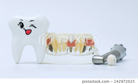 Pediatric dentistry concept featuring a cute winking tooth mascot toy, transparent educational jaw implant model, and clinical handpiece. Pediatric dentistry concept featuring a cute winking tooth mascot toy, transparent educational jaw implant model, and clinical handpiece. 142972025