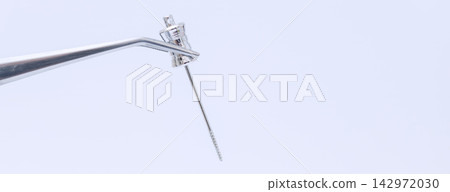 Professional dentistry concept showing a surgical instrument and endodontic file held by tweezers on a wide panoramic background for text. 142972030