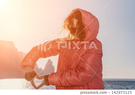 Woman Heart Sunset woman in pink puffer jacket making heart gesture with gloved hands by mountains and sea Woman Heart Sunset woman in pink puffer jacket making heart gesture with gloved hands by mountains and sea 142973125