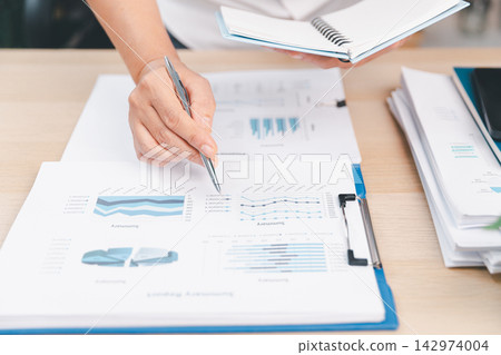 Business professional pointing at financial charts with a pen while holding a notebook, representing data analysis, sales performance, accounting, planning, forecasting, research, Business professional pointing at financial charts with a pen while holding a notebook, representing data analysis, sales performance, accounting, planning, forecasting, research, 142974004