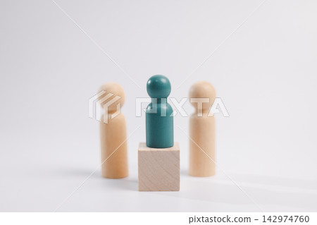 Teal wooden figure standing on a block between two people, representing leadership, recruitment, candidate selection, promotion, management, talent, career opportunity, confidence, and success. Teal wooden figure standing on a block between two people, representing leadership, recruitment, candidate selection, promotion, management, talent, career opportunity, confidence, and success. 142974760