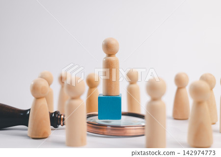 Wooden leader stands on a blue block above a magnifying glass, surrounded by people, representing recruitment, talent selection, leadership, promotion, hiring, and career advancement. 142974773