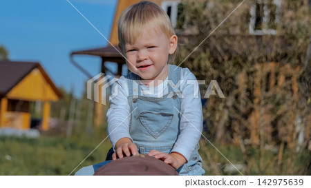 Toddler boy smiling while playing outdoors on wooden seesaw in sunny backyard, with toddler, boy, child, smiling detail, showing playing, seesaw, playground, overall context, with clear visible detail Toddler boy smiling while playing outdoors on wooden seesaw in sunny backyard, with toddler, boy, child, smiling detail, showing playing, seesaw, playground, overall context, with clear visible detail 142975639