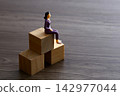 Businesswoman figurine sitting on wooden blocks representing career growth 142977044