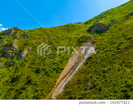 Grassy Mountain Slope with Dry Iron mineral Seep Under Blue Sky Grassy Mountain Slope with Dry Iron mineral Seep Under Blue Sky 142977821