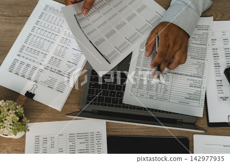 Businessman top view printed financial reports over laptop, checking accounting figures and business records for financial report review and data analysis. Businessman top view printed financial reports over laptop, checking accounting figures and business records for financial report review and data analysis. 142977935