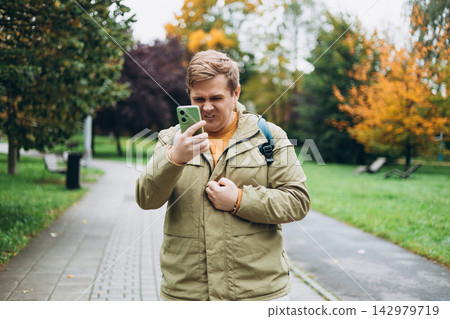 Perplexed man holding cellphone in hands on the street, looking at screen with irritated expression, made a mistake or annoyed by texts and calls. Negative emotion. High quality photo 142979719