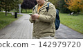 Handsome young 30s man with backpack using mobile phone, texting on smartphone outdoor in park. Technology and communication banner. Autumn time, no face 142979720