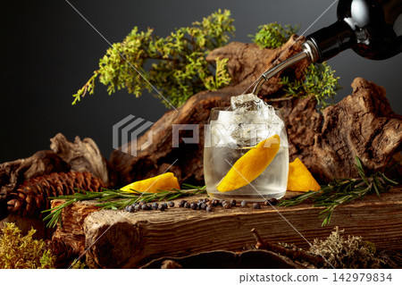 Gin is poured from a bottle into a glass with ice and lemon slice. Gin is poured from a bottle into a glass with ice and lemon slice. 142979834