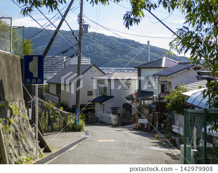 A view of a sloping road leading down through a residential area. A view of a sloping road leading down through a residential area. 142979908