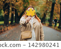 Portrait of pretty young 30s woman in evening autumn park, smiling. Autumn landscape, calmness, tranquility concept. Pretty female holding leaf on nature background. High quality photo. 142980241