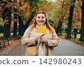 Portrait of pretty young 30s woman in evening autumn park, smiling. Autumn landscape, calmness, tranquility concept. Pretty female holding leaf on nature background. High quality photo. 142980243