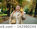 Portrait of pretty young 30s woman in evening autumn park, smiling. Autumn landscape, calmness, tranquility concept. Pretty female holding leaf on nature background. High quality photo. 142980244