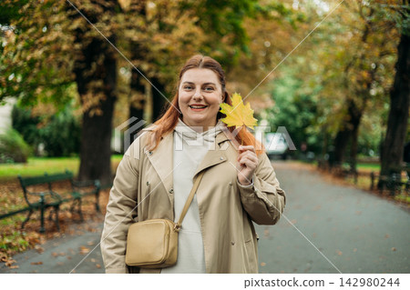 Portrait of pretty young 30s woman in evening autumn park, smiling. Autumn landscape, calmness, tranquility concept. Pretty female holding leaf on nature background. High quality photo. Portrait of pretty young 30s woman in evening autumn park, smiling. Autumn landscape, calmness, tranquility concept. Pretty female holding leaf on nature background. High quality photo. 142980244