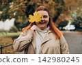 Portrait of pretty young 30s woman in evening autumn park, smiling. Autumn landscape, calmness, tranquility concept. Pretty female holding leaf on nature background. High quality photo. 142980245