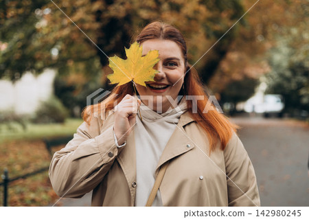 Portrait of pretty young 30s woman in evening autumn park, smiling. Autumn landscape, calmness, tranquility concept. Pretty female holding leaf on nature background. High quality photo. Portrait of pretty young 30s woman in evening autumn park, smiling. Autumn landscape, calmness, tranquility concept. Pretty female holding leaf on nature background. High quality photo. 142980245
