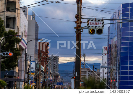A cityscape viewed from a low angle, with streetcar signals and a complex network of overhead wires intersecting in the twilight. A cityscape viewed from a low angle, with streetcar signals and a complex network of overhead wires intersecting in the twilight. 142980397